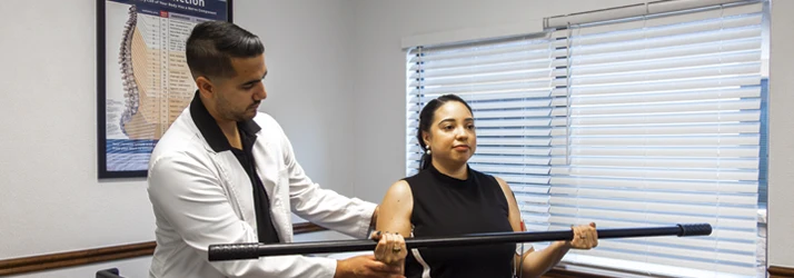 Dr. Jorge Ayala guides a patient through an assisted bar‑lifting exercise to improve mobility and strength.